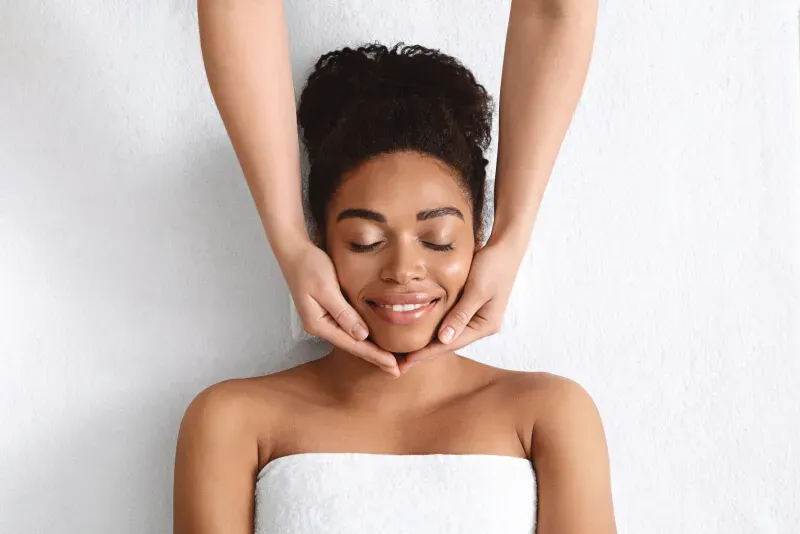 Botox provider touches the face of a black woman wrapped in towel