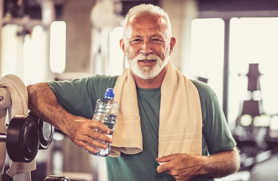 Smiling older man at the gym with a towel and water bottle
